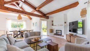 A spacious living room with a fireplace, a television, and a dining area with natural light.