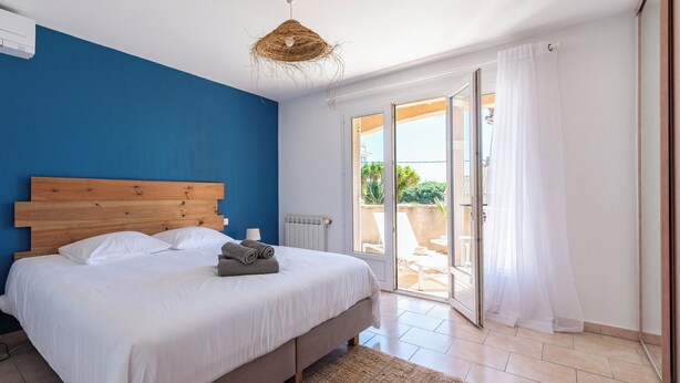 Una camera da letto con una testiera in legno, un letto grande con lenzuola bianche, una lampada a soffitto intrecciata e una porta a vetri scorrevoli che dà su uno spazio all'aperto.