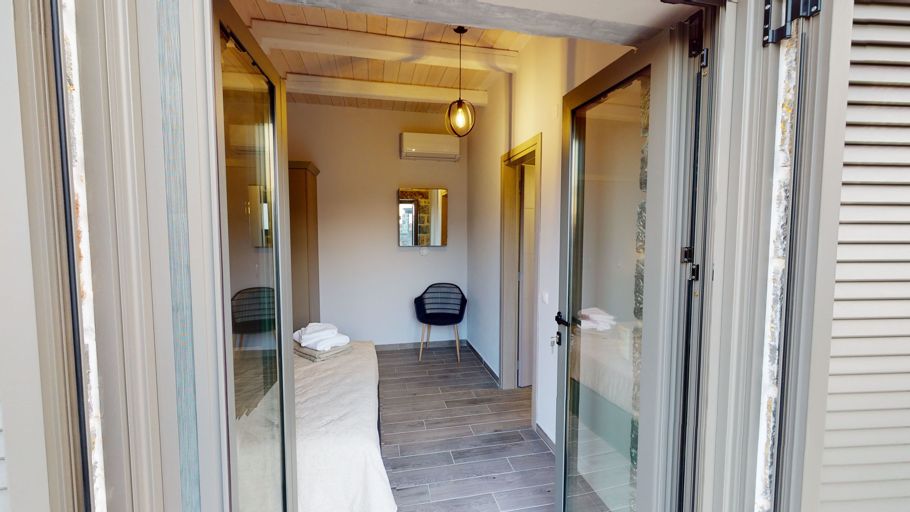 A hallway with a bed, a chair, and a hanging light fixture.