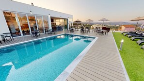 Un área de piscina moderna al aire libre con terraza de madera, sillones de descanso y mesas.
