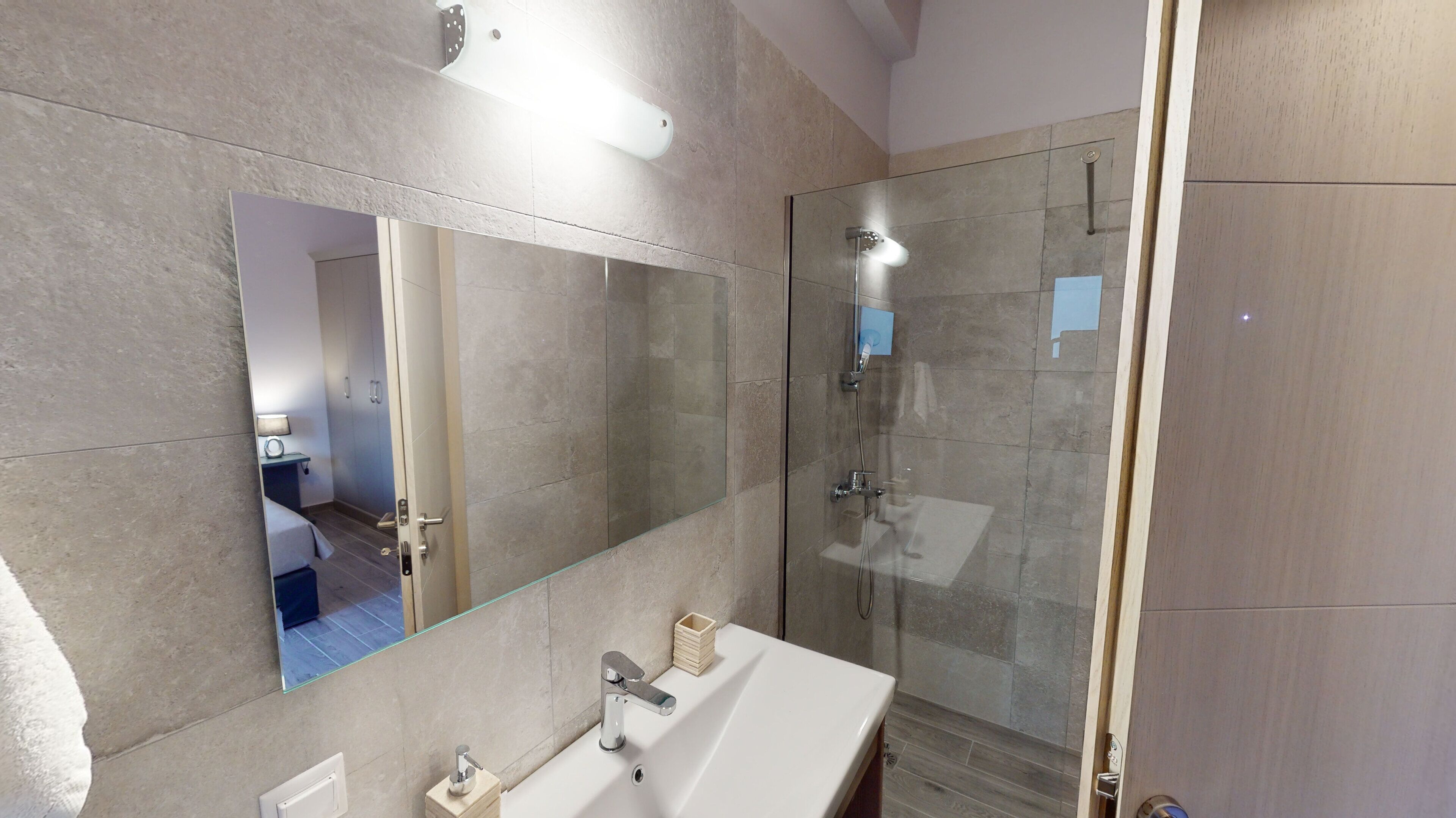 Une salle de bain moderne avec un grand miroir, une douche à parois de verre et un lavabo blanc.