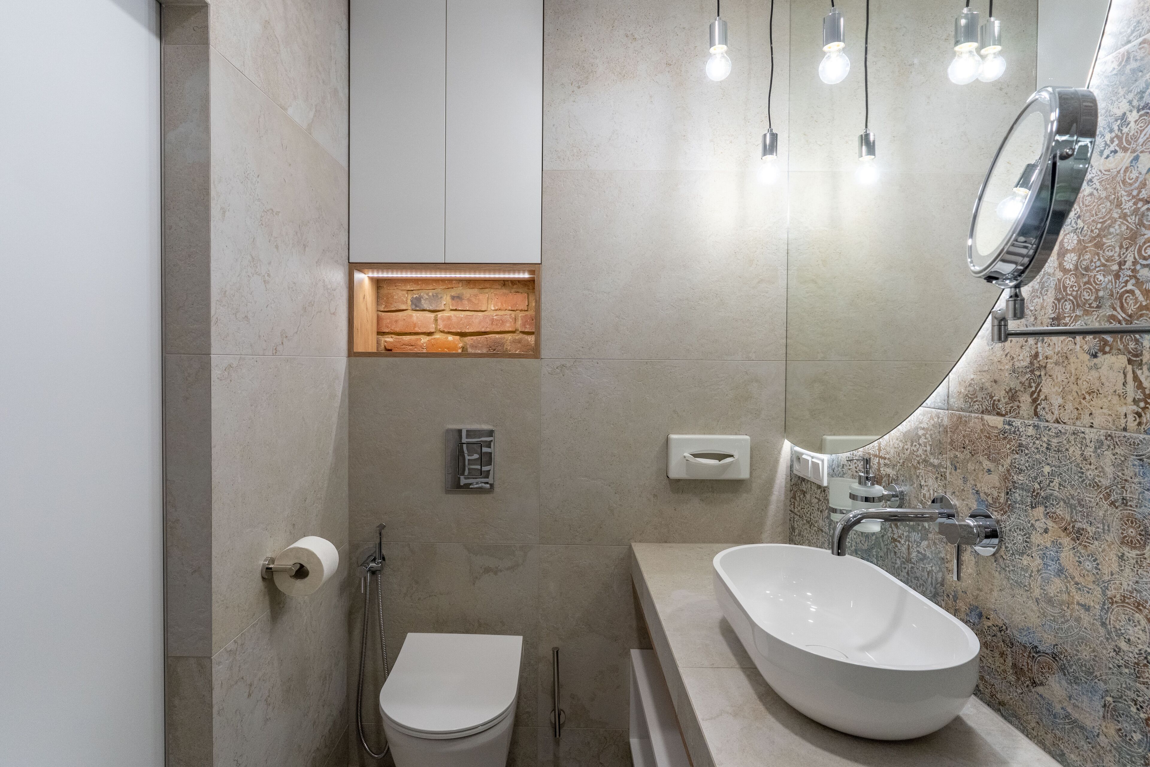Une salle de bain moderne avec des toilettes blanches, une douche intégrée, un grand lavabo ovale et un miroir avec des lumières au-dessus.