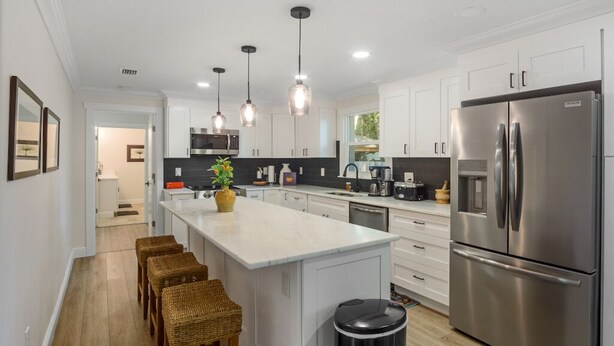 Una cocina moderna con gabinetes blancos, electrodomésticos de acero inoxidable y una isla central con taburetes de bar.