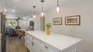 Una cocina moderna con armarios blancos, iluminación colgante y obras de arte en las paredes.
