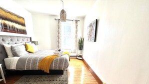 A modern bedroom with a large bed, a bedside table, a chair, and a window with curtains.