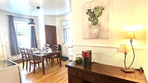 A dining area with a wooden table and chairs, a coffee machine, and a lamp on a dresser.