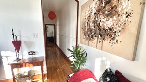 A room with a wooden floor, a desk with a basket, a red umbrella, a plant, and a large abstract painting.