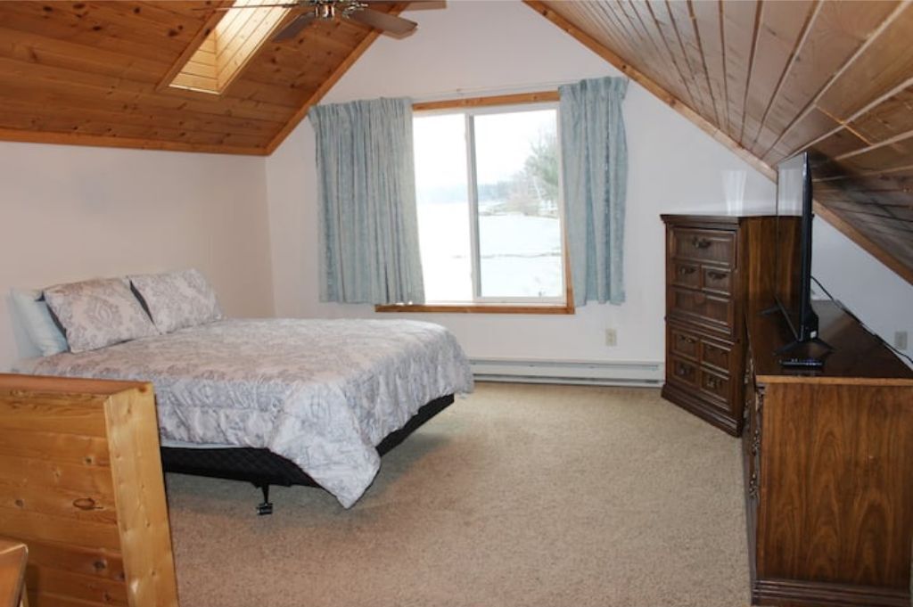 A bedroom with a bed, wooden dresser, and a window with curtains.