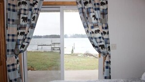 Ein Schlafzimmer mit einem Bett, einem Fenster mit Vorhängen mit Bärenmuster und Blick auf ein Gewässer und einen Steg.