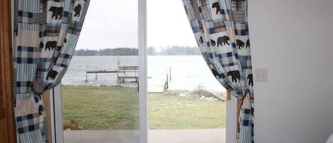 Ein Schlafzimmer mit einem Bett, einem Fenster mit Vorhängen mit Bärenmuster und Blick auf ein Gewässer und einen Steg.