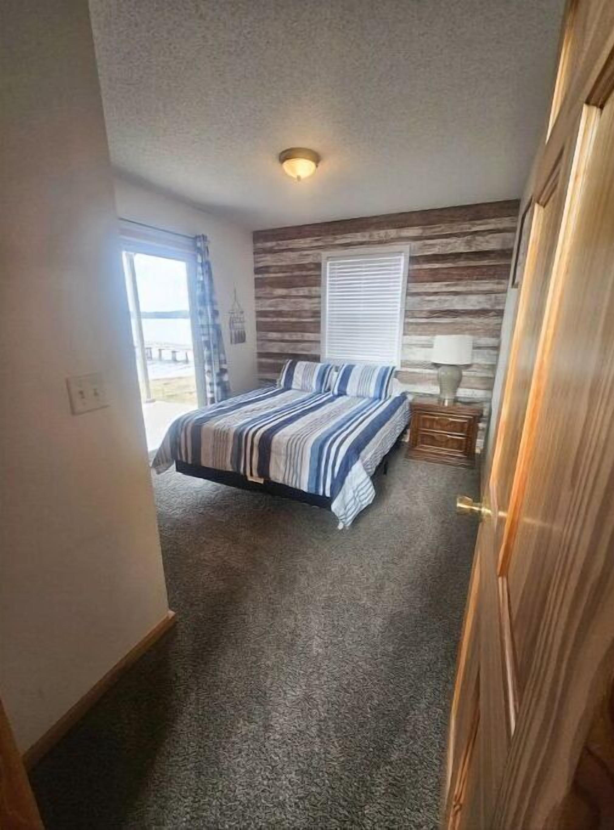 A bedroom with a bed, a nightstand, a lamp, a window with blinds, and a ceiling light.