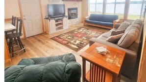 Ein gemütliches Wohnzimmer mit Kamin, Fernseher und großem Fenster mit Seeblick.