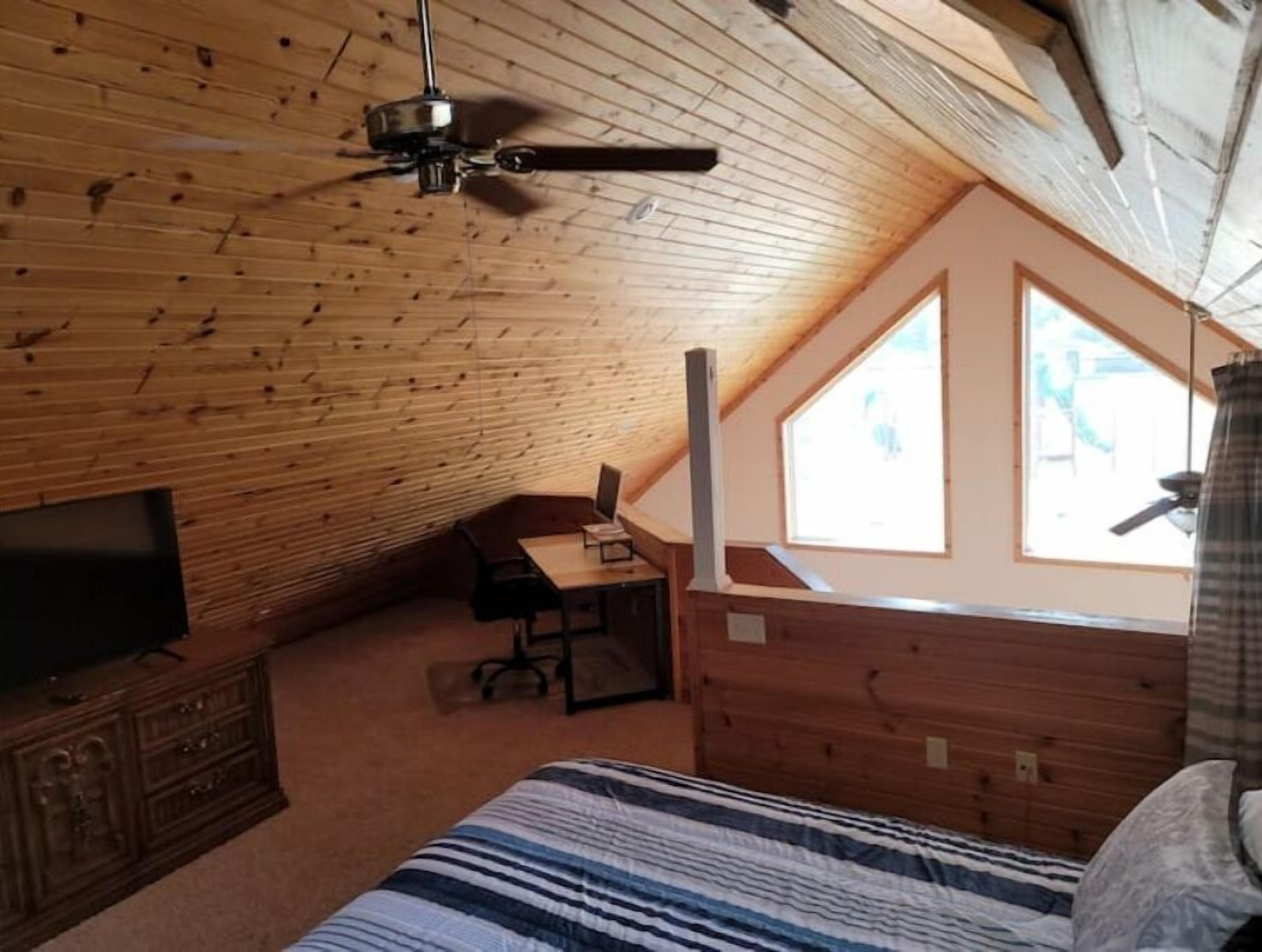 Ein gemütliches Schlafzimmer im Dachgeschoss mit schrägem Dach, einem Bett, einem Schreibtisch und einem Fernseher.