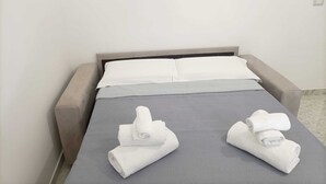 A neatly made bed with grey bedding and two rolled towels on the footboard. - Newhouse Class (Bari)