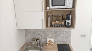 A kitchen with a microwave, tea & coffee box, and a coffee maker on the shelf. - Newhouse Class (Bari)
