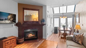 A living room with a fireplace, wooden furniture, and a large window offering a view.