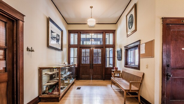 A hallway with wooden floors, a bench, a display case, and a large wooden door. - Historic High School - Stays and events close to skiing, golf, fishing, hunting! (Kingston)