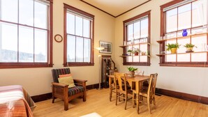 A cozy room with a wooden floor, a dining table with chairs, a sofa with a striped cushion, and large windows with shelves above. - Historic High School - Stays and events close to skiing, golf, fishing, hunting! (Kingston)