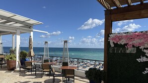 A terrace with tables and chairs, overlooking a beach and the sea. - Exclusive 3 Bedrooms Apartment W/ Amazing View (Hallandale Beach)
