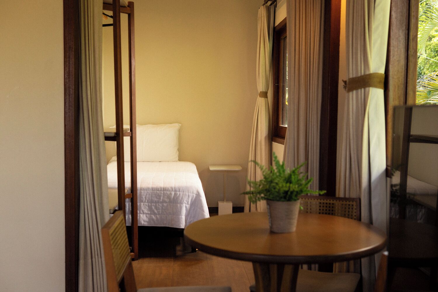 Una habitación estrecha con una cama, una mesa con una planta en maceta y una silla.