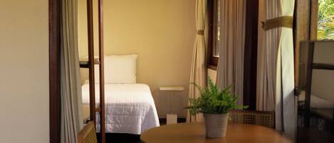 Una habitación estrecha con una cama, una mesa con una planta en maceta y una silla.