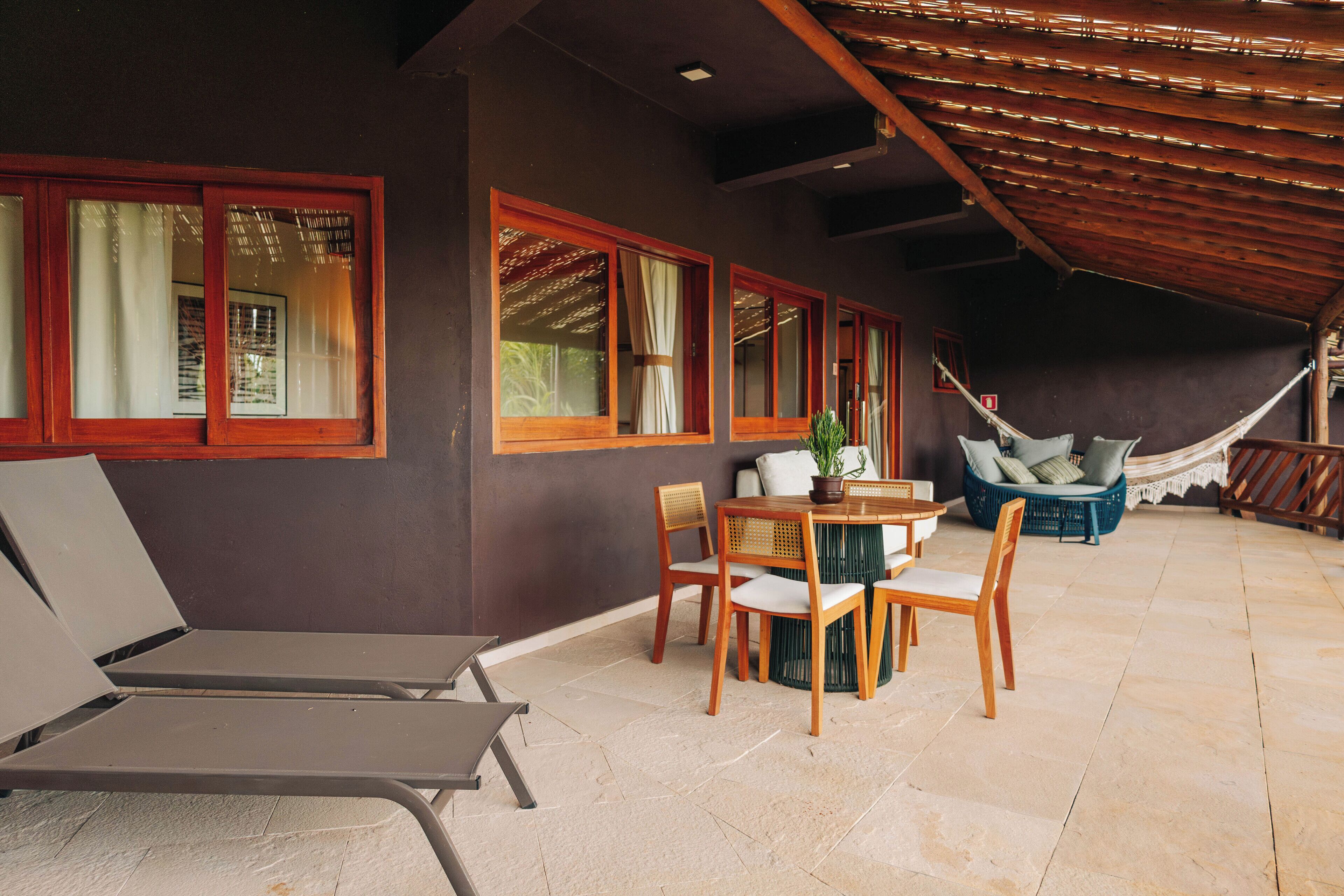 A covered outdoor seating area with a table and chairs, a hammock, and a view of the surrounding landscape.