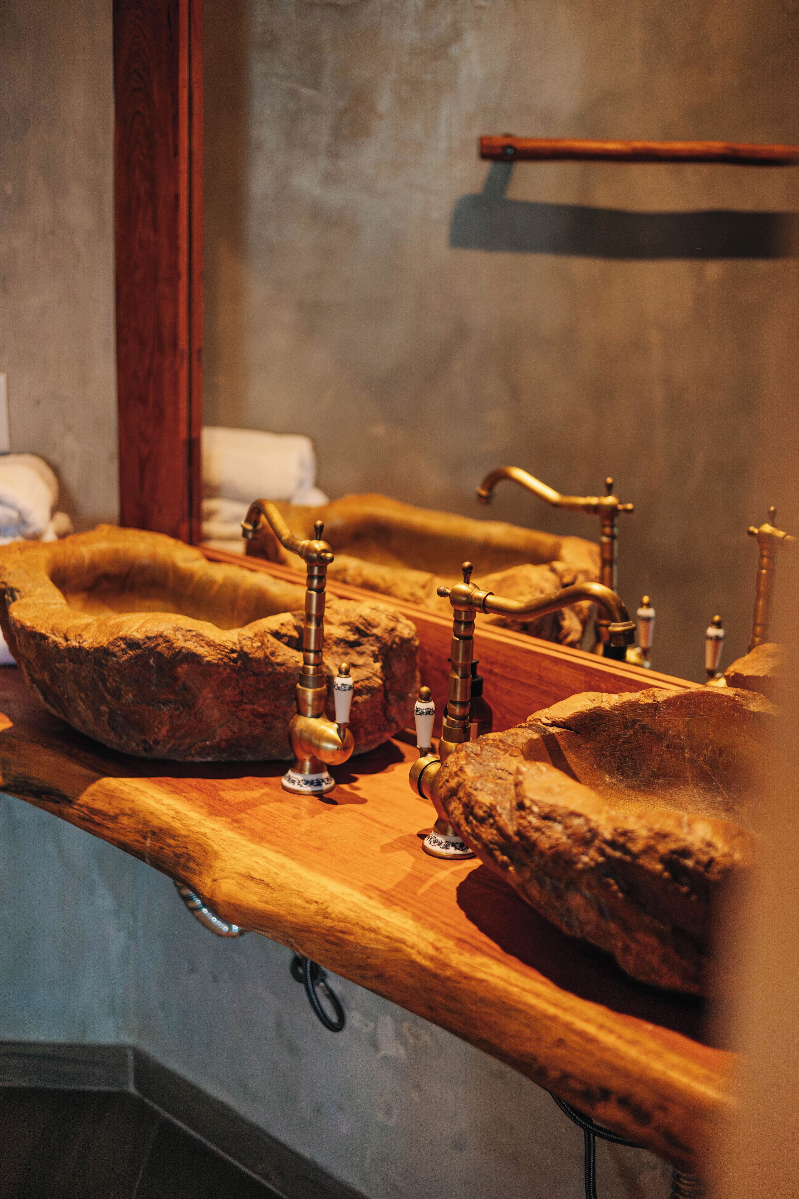 Un baño con diseño rústico, que incluye un lavamanos grande de madera y múltiples grifos.