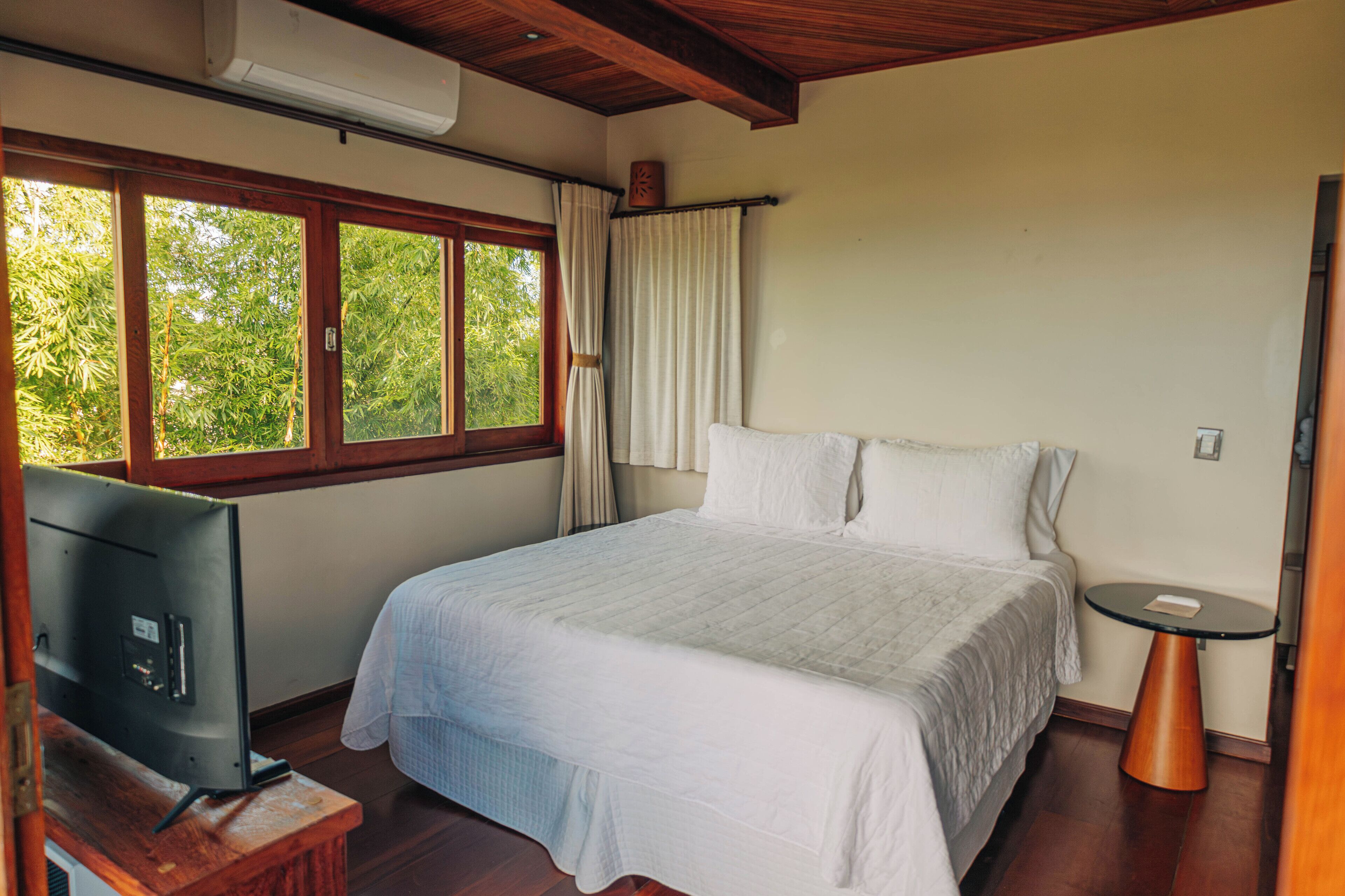 A bedroom with a bed, a TV, and a window with curtains.