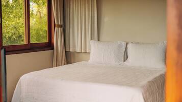 Una cama bien hecha con sábanas blancas en una habitación con un ventanal y cortinas.