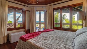 A bedroom with a large bed, a bench, and a view of the ocean. - Chocolate Hotel (Itacaré)