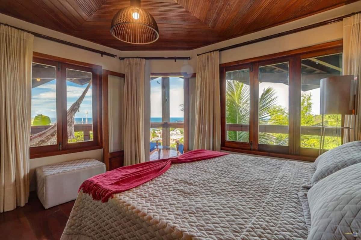 Una camera da letto con un letto grande, una panca e vista sull'oceano.