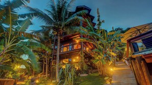 A multi-story building with a staircase leading to the upper levels, surrounded by lush tropical vegetation. - Chocolate Hotel (Itacaré)