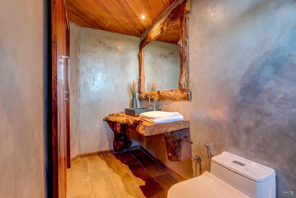Een badkamer met een rustieke inrichting, met een houten wastafelmeubel, een grote spiegel en een wit toilet.
