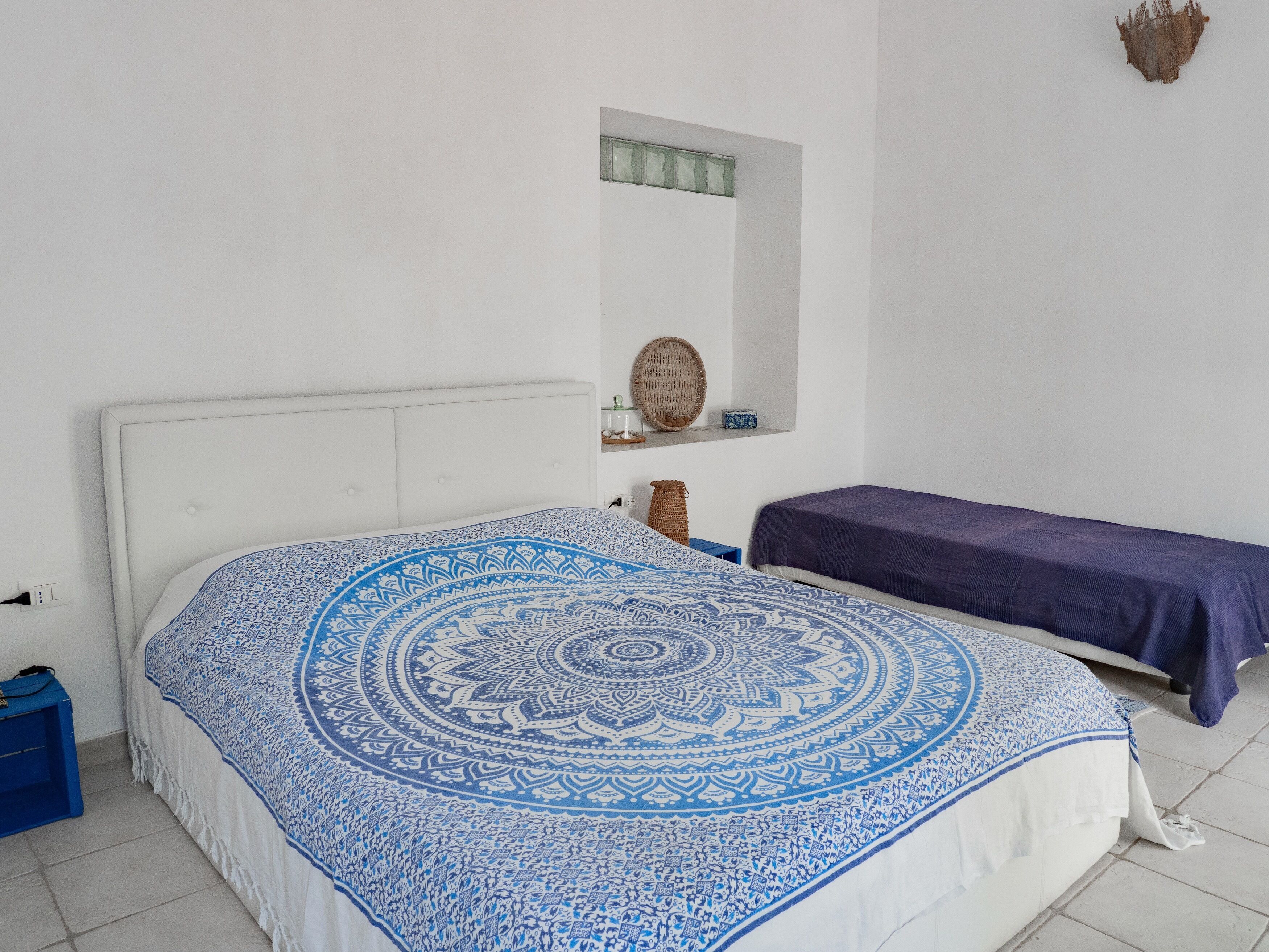 Un dormitorio con una cama grande, una cama más pequeña, una ventana y un estante con objetos decorativos.