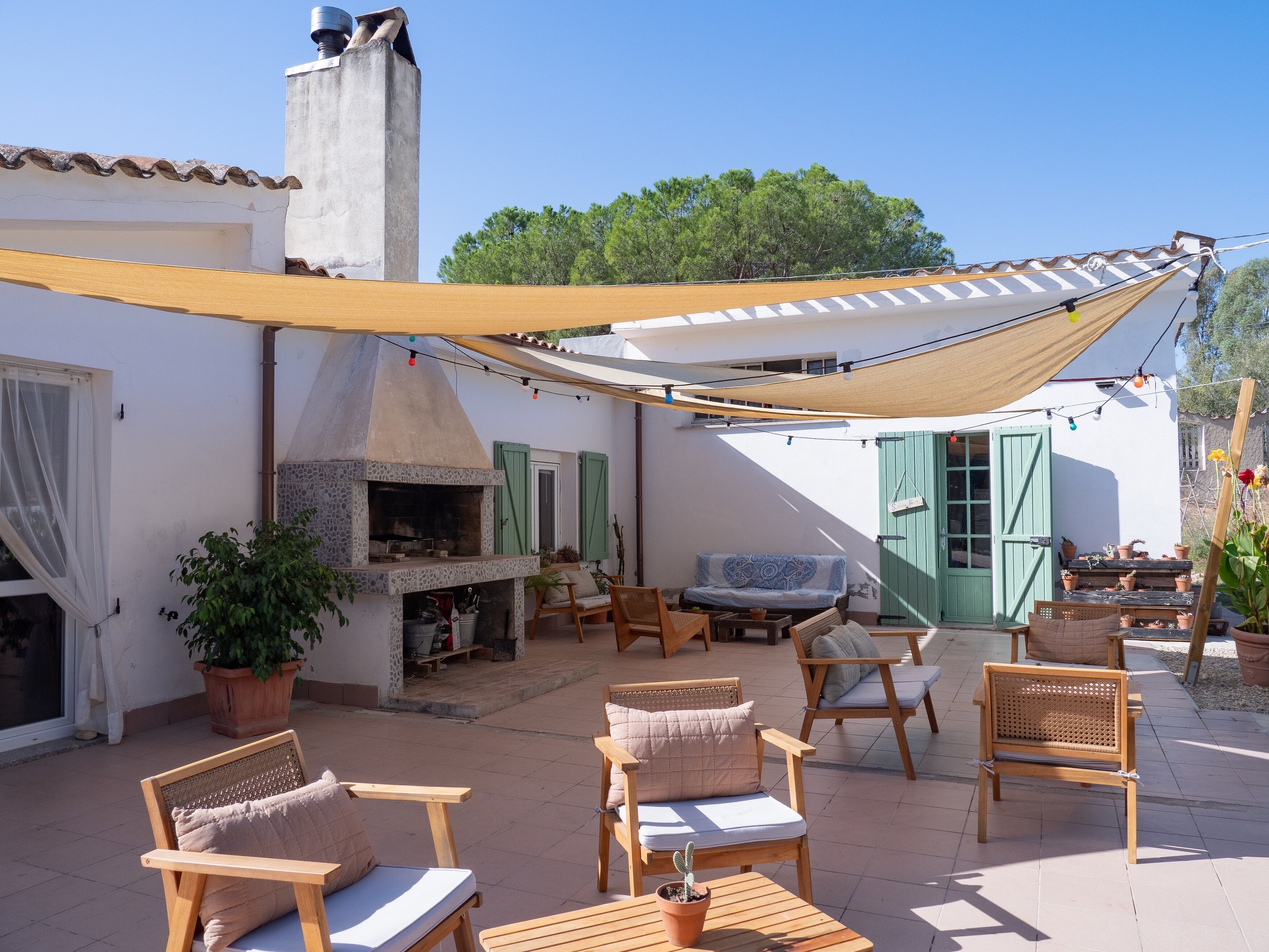 An outdoor patio with wooden furniture, a stone fireplace, and a pergola providing shade.