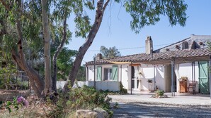 A rustic house with a tiled roof, a paved driveway, and a garden with rocks and plants. - Domu Prexada (Maracalagonis)