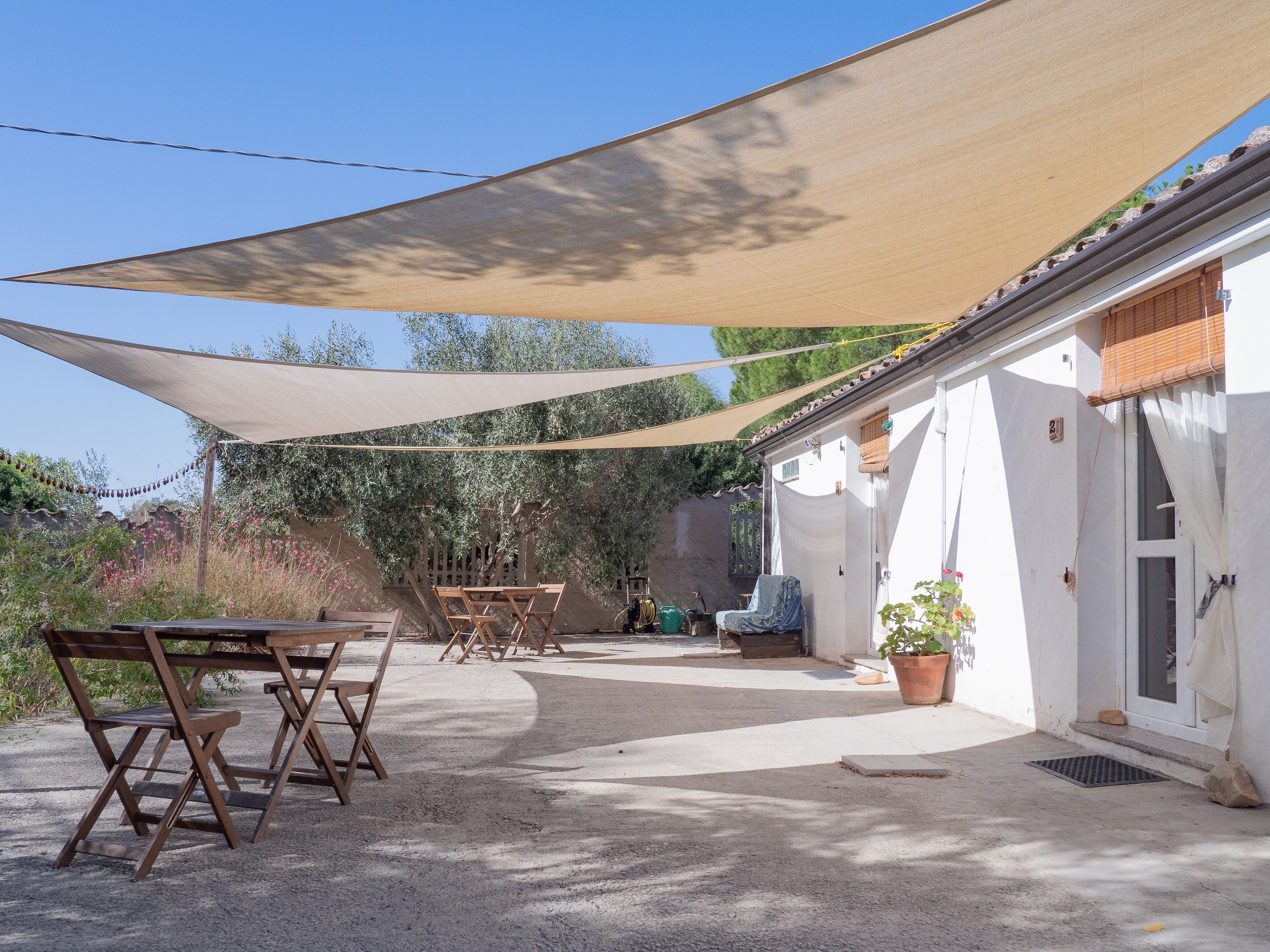 A patio area with a table and chairs, a large shade sail, and a building with a tiled roof.