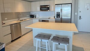 A modern kitchen with white cabinetry, stainless steel appliances, and a central island with stools. - 37a Exceptional 2 bedroom PH Incredible View (Hallandale Beach)