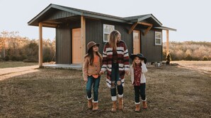 Une famille se tient devant une maison en bois dotée d’un porche.