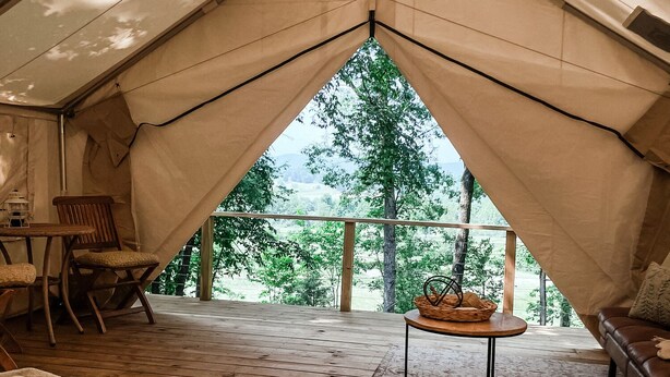 Un hébergement sous tente comprenant un lit, une table avec un panier, et offrant une vue sur les arbres et les collines.