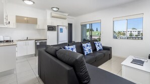 A modern apartment with a kitchen, a black leather sofa with floral cushions, and a view of the neighborhood through large windows. - Stylish Unit with Water Views (BELLARA)