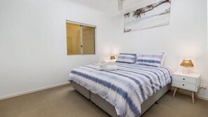 A bedroom with a bed, a nightstand, a lamp, a window, and a painting on the wall. - Stylish Unit with Water Views (BELLARA)