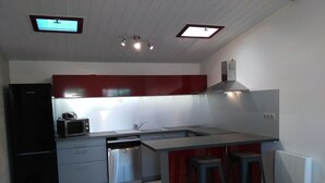 Een moderne keuken met roestvrijstalen apparatuur, een rode accentmuur en een vast kookeiland met krukken.