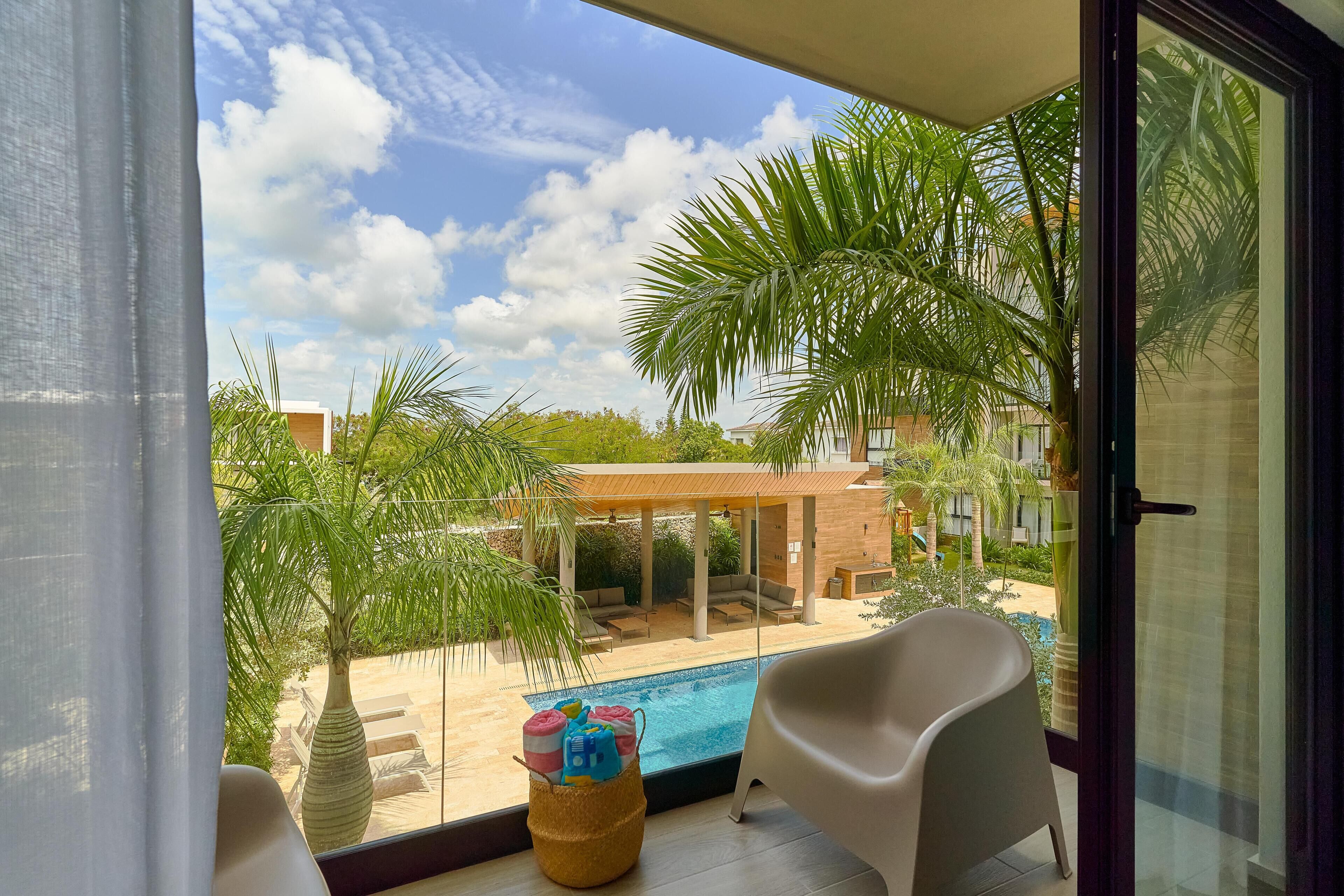 Een balkon met uitzicht op een zwembad, palmbomen en een overdekt zitgedeelte.