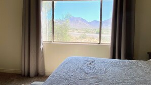 Ein Zimmer mit einem Bett, einem Fenster und Blick auf Berge und eine Wüstenlandschaft.