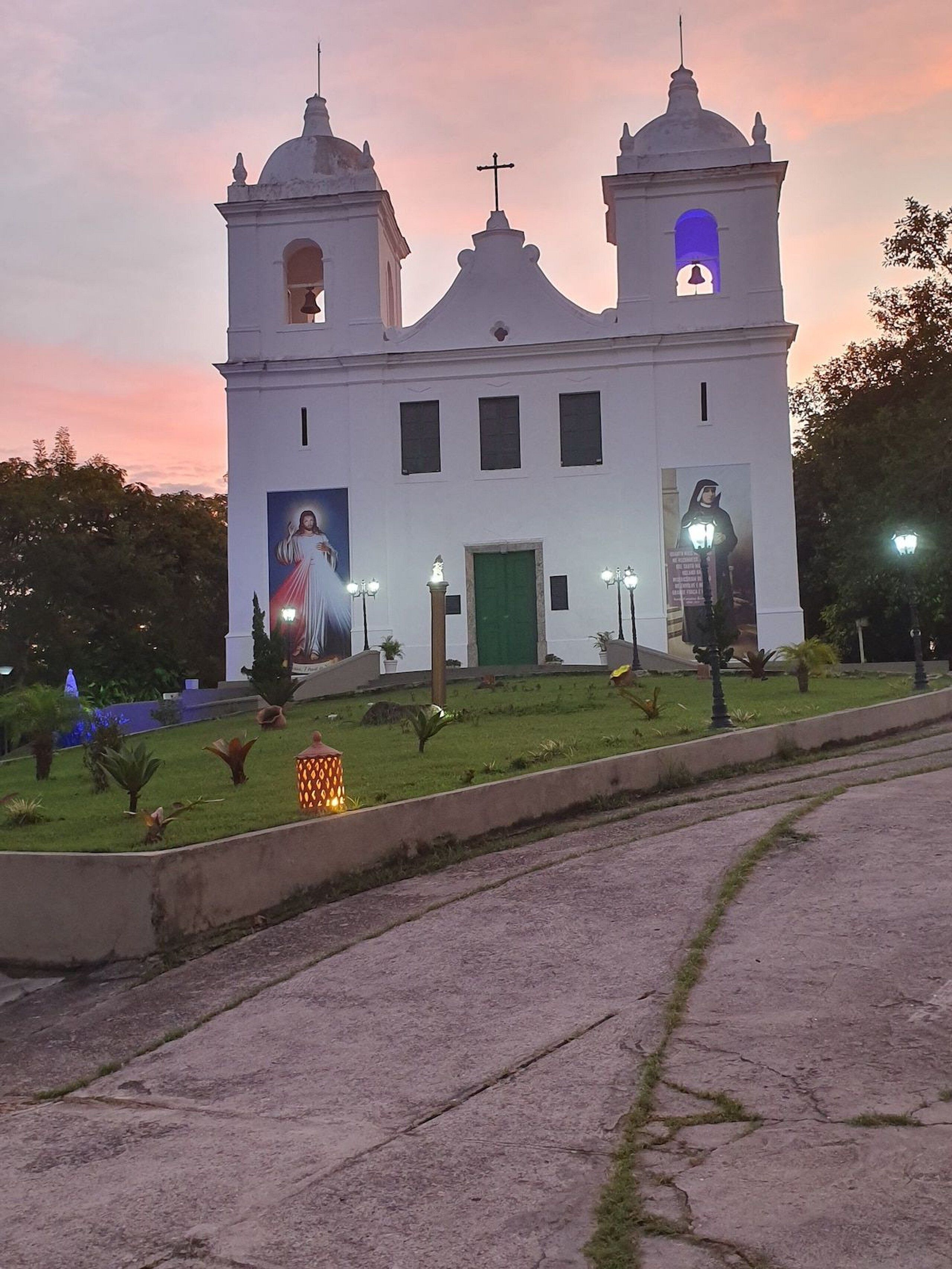 En hvid kirke med to kirketårne og en central kuppel, med et stort religiøst muralmaleri og en grøn dør.