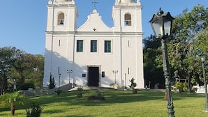 A white church with two bell towers and a central entrance, surrounded by a well-maintained lawn and a few trees. - Andorinhas (Niteroi)