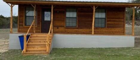 A wooden cabin with a porch and a single staircase leading to the entrance.