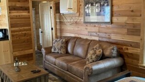 Et interiør af en træhytte med en brun lædersofa, et lille træbord og et billede i ramme på væggen.