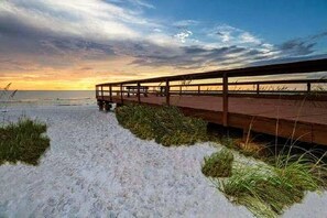 A wooden boardwalk leading to a beach with sand and grass in the foreground. - Furnished, LARGE 1 Bedroom, 1 Bath BEACHFRONT Condo on #1 Beach in the U.S   (Clearwater)